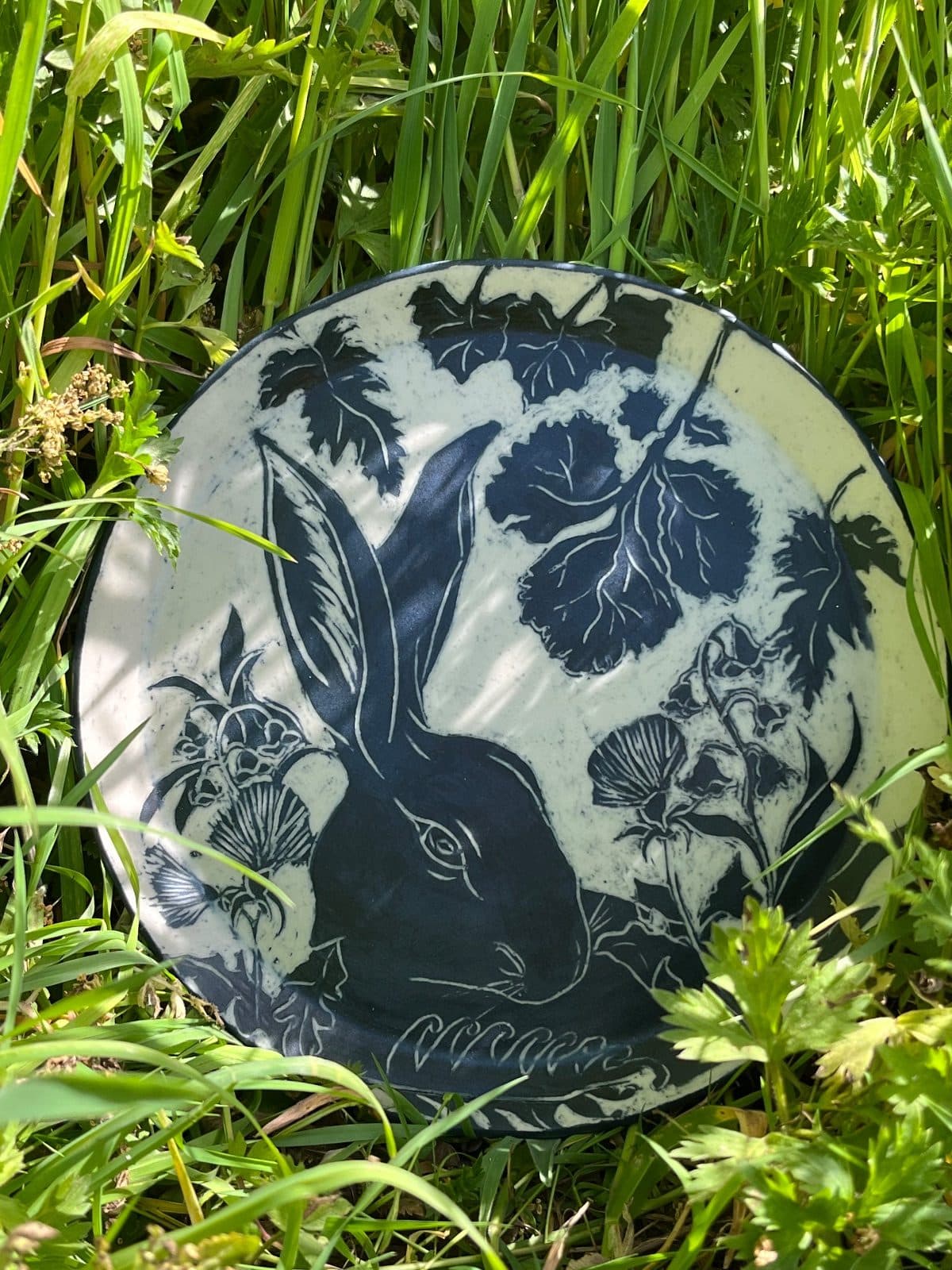 A stoneware plate with a sgraffito hare among leaves, set in long grass