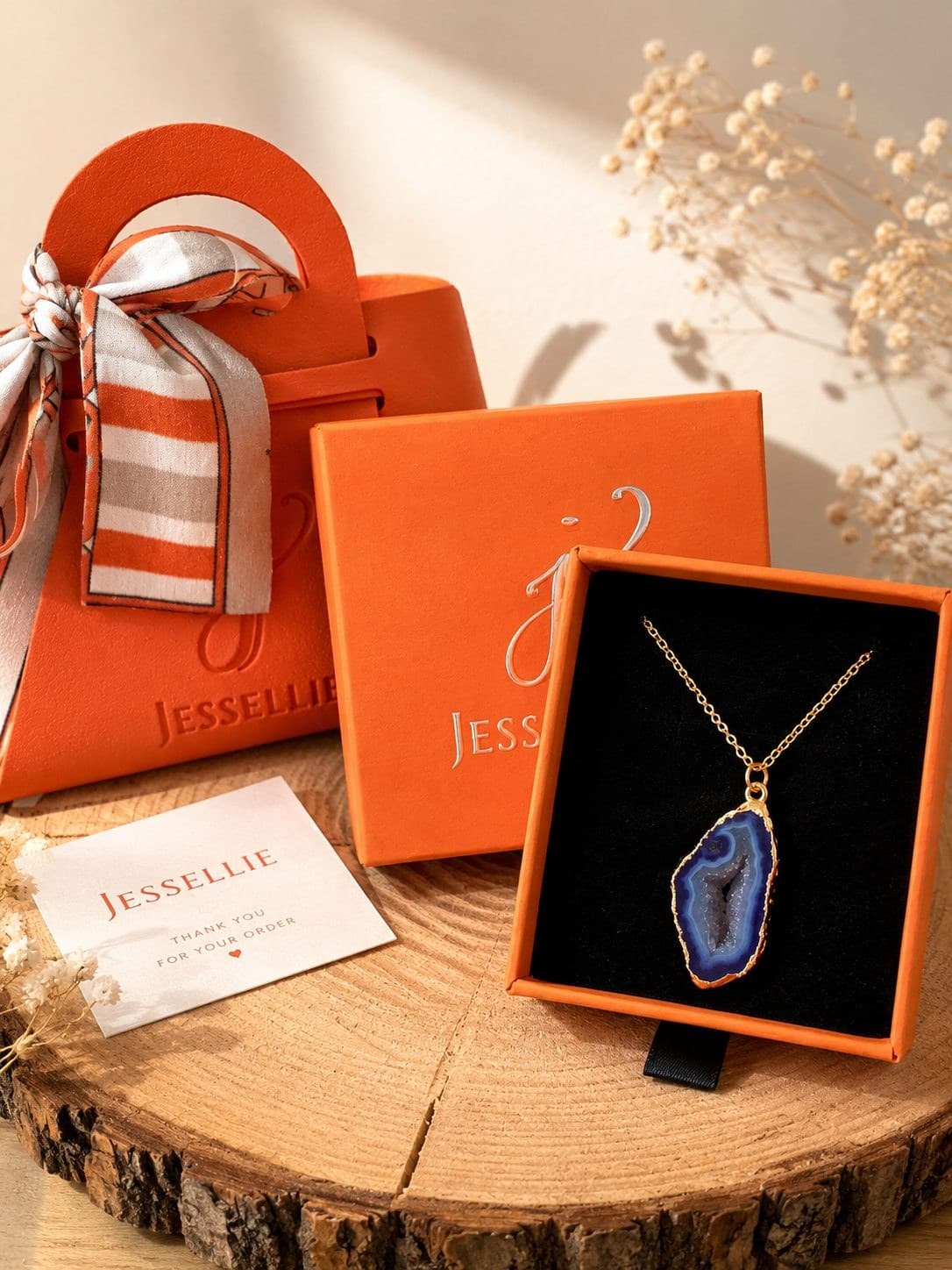 A wire-wrapped agate pendant in a Jessellie gift box on a wooden slice