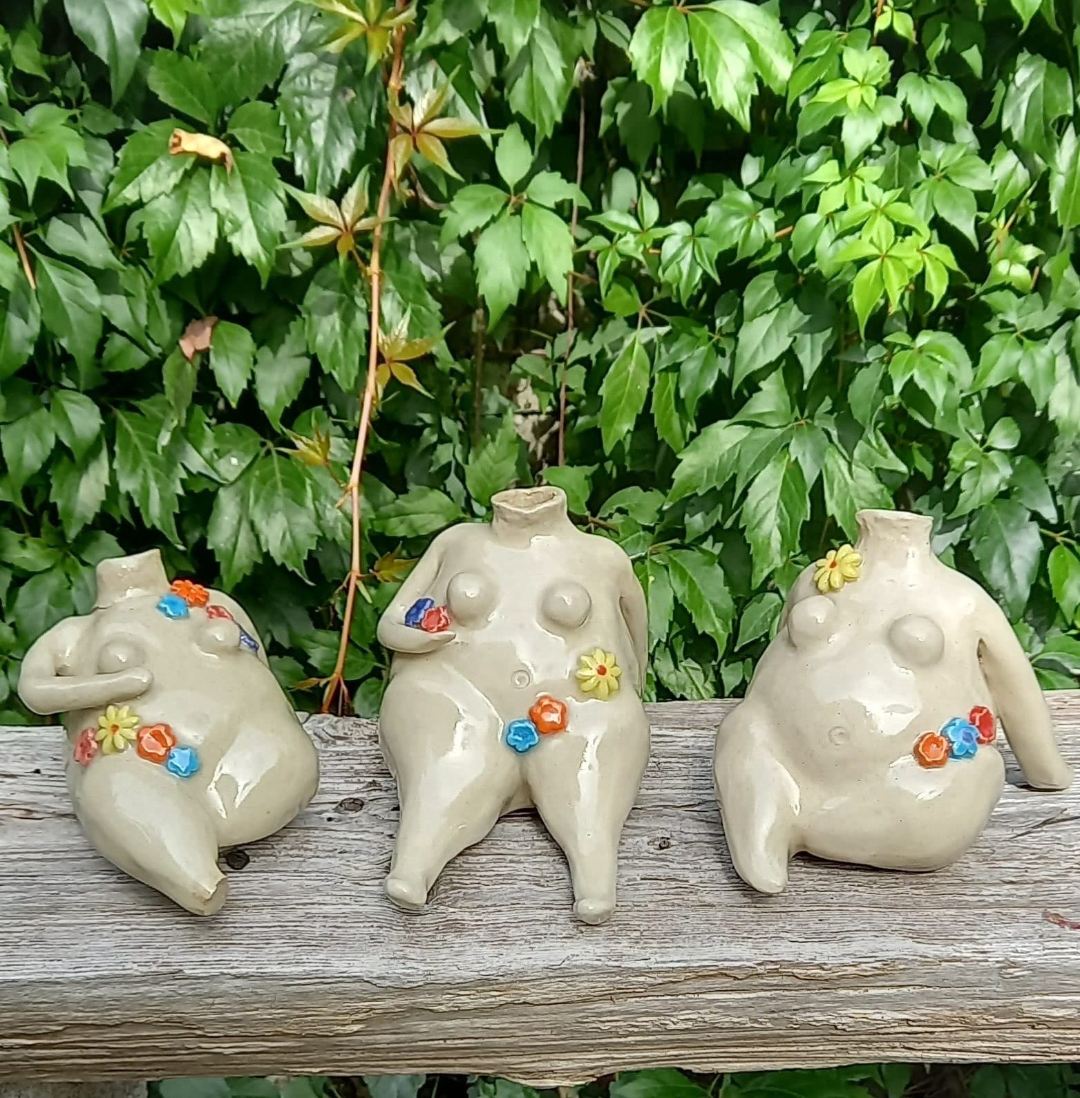 Three ceramic figures with coloured dot detailing, sitting on a garden wall