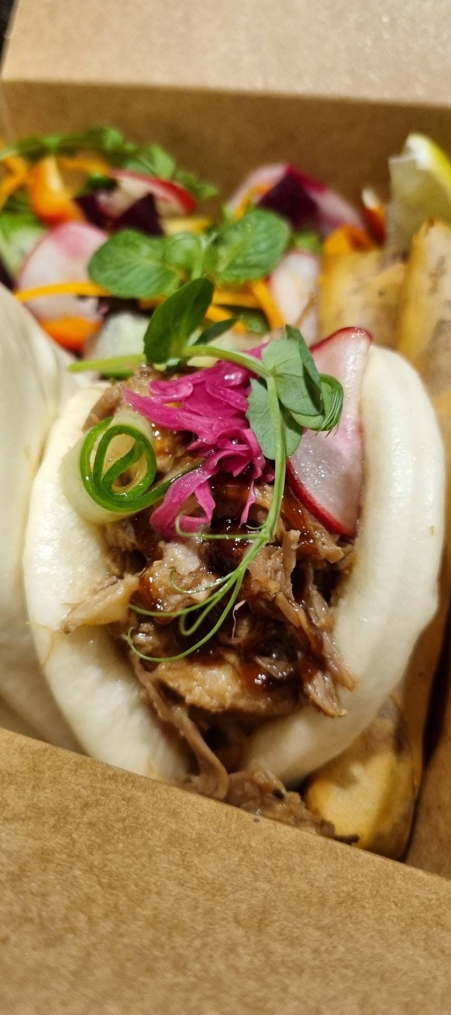 A freshly steamed bao bun piled with glazed filling and fresh garnish